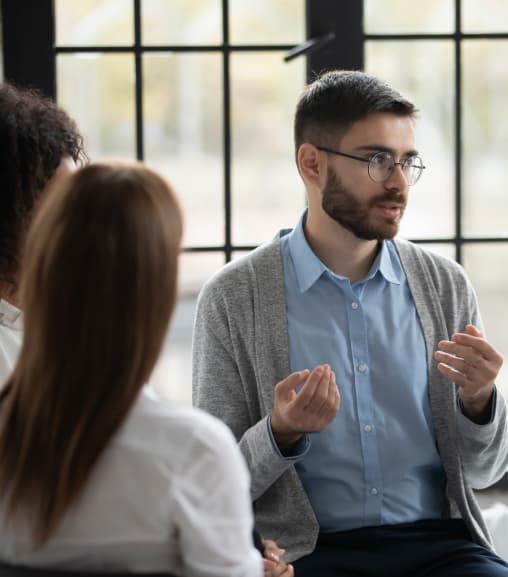 A Man Discusses With Two Women At A Table With Documents And Laptops During A Meeting