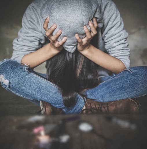 A Distressed Woman Sits On The Floor, Covering Her Face With Her Hands In A Drug Rehabilitation Setting