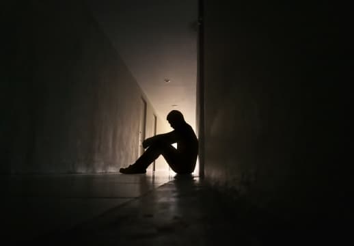 A Person Sitting Alone In A Dim Hallway, Conveying A Somber Atmosphere