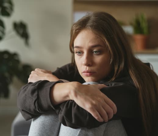 A Young Woman Sits On A Couch, Appearing Sad And Reflective In Her Living Room