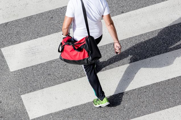 A Man In A White Shirt Crosses The Street With A Red Bag