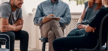 A Diverse Group Of People Seated In Chairs, Engaged In Casual Conversation
