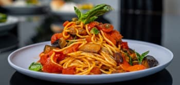 A Plate Of Spaghetti Topped With Vibrant Vegetables And Herbs