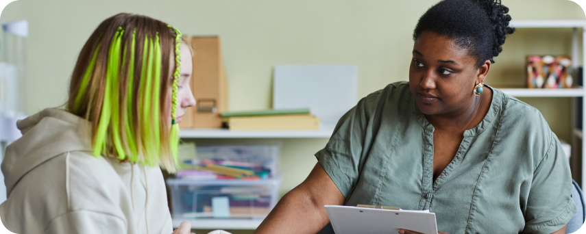A Woman With Green Hair Sits Beside Another Woman In Green Shirt, Conversing