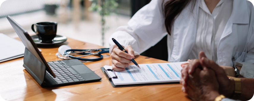 A Doctor Writes Notes On A Clipboard At A Desk In An Office