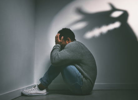 A Man Sits Against A Wall, Casting A Dragon-Shaped Shadow Behind Him
