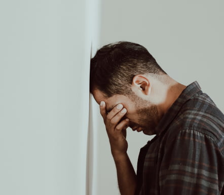 Man Leans Against A Wall, Head In Hands, Showing Stress Or Contemplation