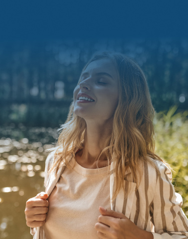 A Joyful Woman Stands By The Water, Sunlight Reflecting On The Surface